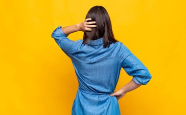 Genç, güzel bir kadın düşünüyor ya da şüphe ediyor, kafasını kaşıyor, kafası karışık ve kafası karışık hissediyor, geriye ya da arkaya bakıyor.