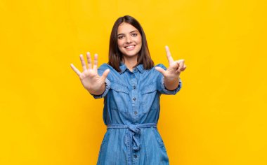 Genç ve güzel bir bayan gülümsüyor ve dost canlısı görünüyor, 7 ya da 7 numarayı gösteriyor, eli önde, geriye doğru sayıyor.