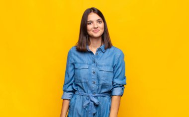 Genç ve güzel bir kadın pozitif ve kendinden emin gülümsüyor. Tatmin olmuş, arkadaş canlısı ve mutlu görünüyor.