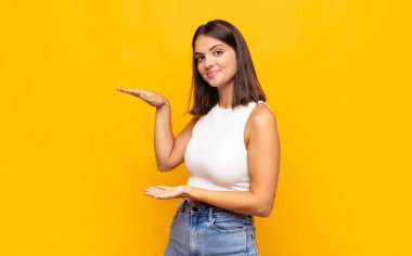 Genç ve güzel bir kadın bir objeyi iki eliyle fotokopi alanında tutuyor, bir objeyi gösteriyor, sunuyor ya da reklamını yapıyor.