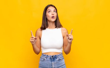 Genç ve güzel bir kadın huşu içinde ve ağzı açık bir şekilde şaşkın ve şaşkın bir bakışla yukarıya bakıyor.