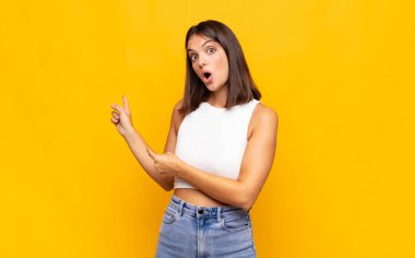 Genç, güzel bir kadın şaşkın ve şaşırmış hissediyor. Yan taraftaki fotokopi alanını işaret ediyor. Şaşırmış, ağzı açık bir bakışla.