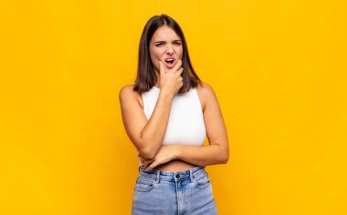 Ağzı ve gözleri açık, eli çenesinde genç ve güzel bir kadın. Hoş olmayan bir şok geçiriyor.