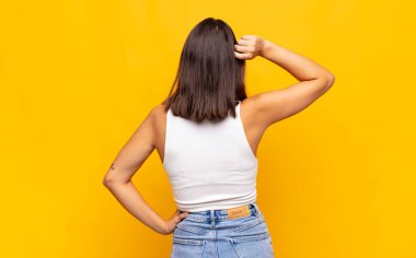 Genç, güzel bir kadın bilgisiz ve kafası karışık hissediyor, bir çözüm düşünüyor, eli kalçasında, diğeri kafasında, dikiz aynasından.