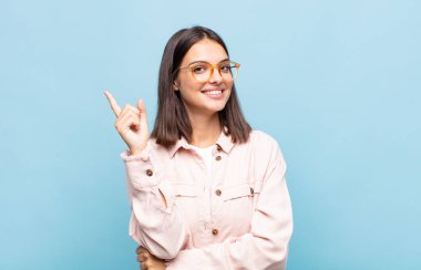 Genç ve güzel bir kadın mutlu bir şekilde gülümsüyor ve yan bakıyor, merak ediyor, düşünüyor ya da bir fikri var.