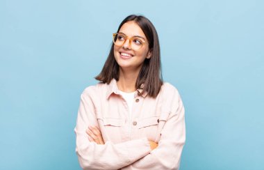 Genç, güzel bir kadın kendini mutlu, gururlu ve umutlu hissediyor, merak ediyor veya düşünüyor, çapraz kollarla boşluğu doldurmaya çalışıyor.