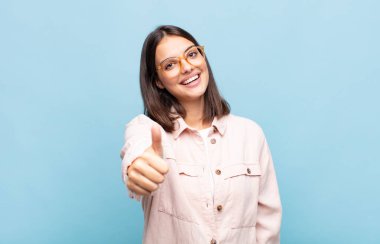 Genç, güzel bir kadın gururlu, tasasız, kendinden emin ve mutlu, başparmağıyla olumlu gülümsüyor.