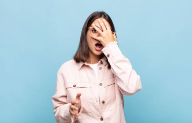 Genç, güzel bir kadın şok olmuş, korkmuş ya da korkmuş görünüyor. Yüzü elle kaplanmış ve parmaklarının arasından gizlice bakıyor.