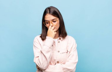 Genç ve güzel bir kadın ciddi, düşünceli ve endişeli, elleri çenesine bastırılmış bir şekilde yan bakıyor.