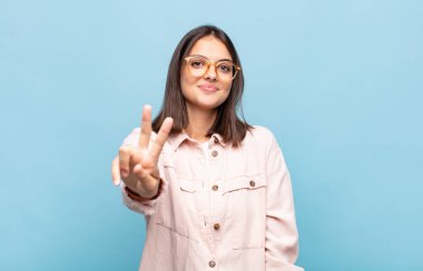 Genç, güzel bir kadın gülümsüyor ve arkadaş canlısı görünüyor. İki ya da iki numarayı gösteriyor. Elleri önde, geri sayıyor.