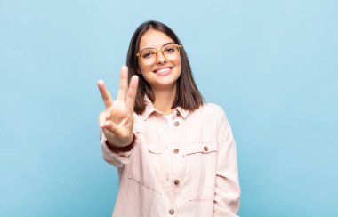 Genç, güzel bir kadın gülümsüyor ve arkadaş canlısı görünüyor. Üç ya da üç numarayı gösteriyor. Elleri önde, geriye doğru sayıyor.