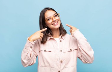 Genç, güzel bir kadın, kendine güvenerek gülümsüyor. Kendi gülüşünü gösteriyor. Olumlu, rahat, tatmin olmuş bir tavır.