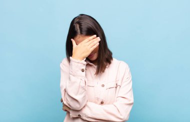 Genç, güzel bir kadın stresli, utanmış ya da üzgün görünüyor. Baş ağrısı var, yüzü elle kapatılmış.