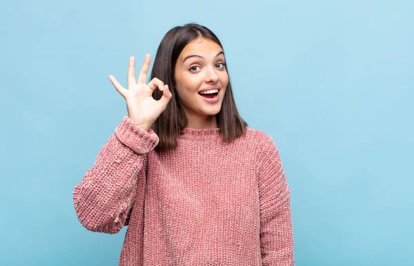 Genç ve güzel bir kadın kendini başarılı ve tatmin olmuş hissediyor, ağzı açık gülümsüyor, elle işaret veriyor.