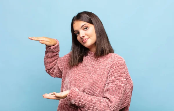 Genç ve güzel bir kadın bir objeyi iki eliyle fotokopi alanında tutuyor, bir objeyi gösteriyor, sunuyor ya da reklamını yapıyor.