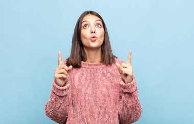 Genç ve güzel bir kadın huşu içinde ve ağzı açık bir şekilde şaşkın ve şaşkın bir bakışla yukarıya bakıyor.