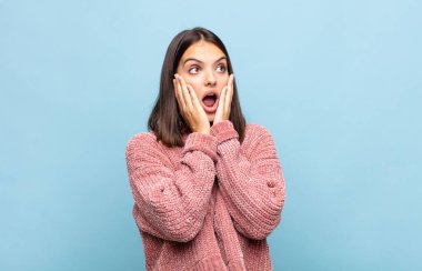 Genç, güzel bir kadın mutlu, heyecanlı ve şaşırmış hissediyor. İki eli de havada bir tarafa bakıyor.