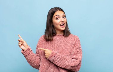 Genç ve güzel bir kadın şaşkın bir ifadeyle gülümsüyor ve bir tarafı işaret ediyor.