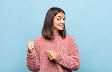 Genç ve güzel bir kadın neşeyle gülümsüyor ve yan taraftaki fotokopi alanını işaret ediyor, mutlu ve tatmin olmuş hissediyor.