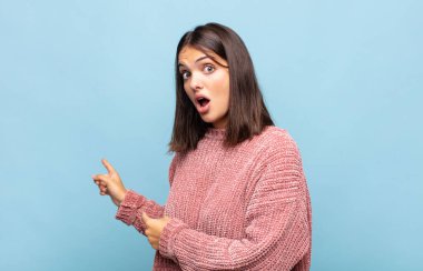 Genç, güzel bir kadın şaşkın ve şaşırmış hissediyor. Yan taraftaki fotokopi alanını işaret ediyor. Şaşırmış, ağzı açık bir bakışla.