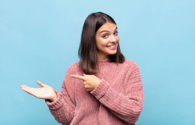 Genç ve güzel bir kadın neşeyle gülümsüyor ve yan taraftaki fotokopi alanına işaret ediyor, bir nesneyi gösteriyor ya da reklamını yapıyor.