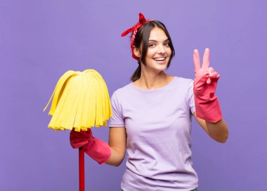 Genç ve güzel bir kadın gülümsüyor ve mutlu görünüyor, arkadaş canlısı ve memnun, işaret eden zafer ya da barış iki elle