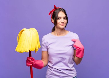 Genç ve güzel bir kadın gururlu, kendinden emin ve mutlu görünüyor, gülümsüyor ve kendini işaret ediyor ya da bir numaralı işareti yapıyor.