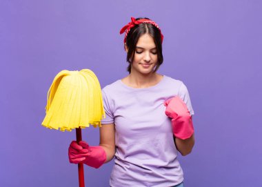 Genç ve güzel bir kadın neşeyle gülümsüyor, yere bakıyor ve göğsüne işaret ediyor.