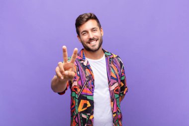Genç adam gülümsüyor ve mutlu görünüyor, kaygısız ve pozitif, tek elle zafer ya da barış işareti yapıyor.
