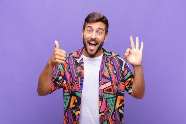 Genç adam mutlu, şaşkın, tatmin olmuş ve şaşırmış hissediyor, iyi görünüyor ve el hareketlerini gösteriyor, gülümsüyor.