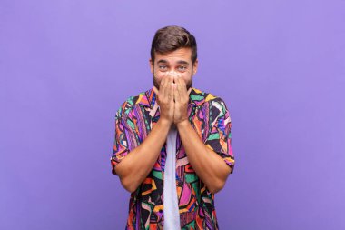 Genç adam mutlu, neşeli, şanslı ve şaşkın görünüyor. İki eliyle ağzını kapatıyor.