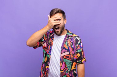 Genç adam şok olmuş, korkmuş ya da korkmuş görünüyor. Yüzü elle örtülmüş ve parmaklarının arasından gizlice bakıyor.