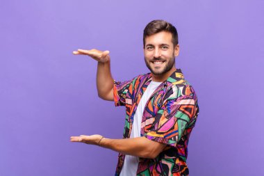 Genç adam gülümsüyor, mutlu, pozitif ve tatmin olmuş hissediyor, fotokopi alanında nesne veya konsept tutuyor veya gösteriyor