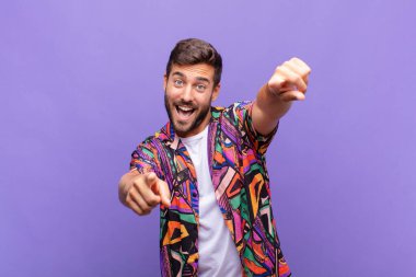 Genç adam mutlu ve kendinden emin, kamerayı iki eliyle gösteriyor ve gülüyor, seni seçiyor.