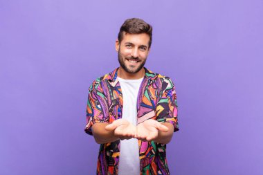 Genç adam mutlu bir şekilde gülümsüyor arkadaş canlısı, kendinden emin, pozitif bakışlı, bir nesne ya da konsept sunuyor ve gösteriyor