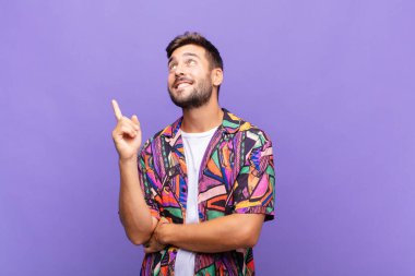 Genç adam mutlu bir şekilde gülümsüyor ve yan bakıyor, merak ediyor, düşünüyor ya da bir fikri var.