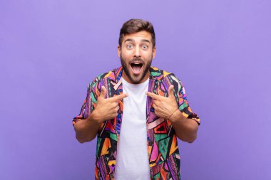 Genç adam mutlu, şaşkın ve gururlu, heyecanlı, şaşkın bakışlarla kendini işaret ediyor.