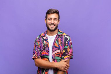 Genç adam utangaç ve neşeli bir şekilde gülüyor, arkadaş canlısı ve olumlu ama güvensiz bir tavırla.