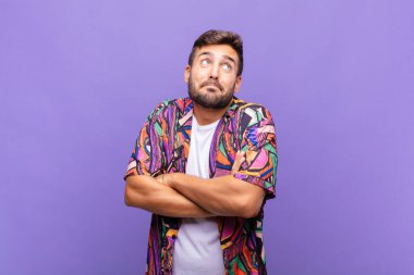 Genç adam omuz silkiyor, kafası karışık ve kararsız, kolları bağlı ve şaşkın bir şekilde şüpheli bakıyor.