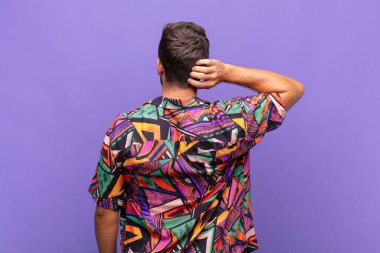 Genç adam düşünüyor ya da şüphe ediyor, kafasını kaşıyor, kafası karışık ve kafası karışık hissediyor, geriye ya da arkaya bakıyor.