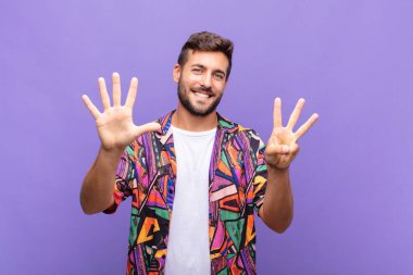 Genç adam gülümsüyor ve arkadaş canlısı görünüyor, 8 ya da 8 numarayı gösteriyor, elleri önde, geriye doğru sayıyor.