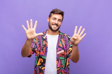 Genç adam gülümsüyor ve dost canlısı görünüyor, 9 ya da 9 numarayı gösteriyor, eli önde, geriye doğru sayıyor.