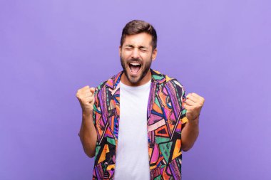 Genç adam son derece mutlu ve şaşırmış görünüyor, başarıyı kutluyor, bağırıyor ve zıplıyor.