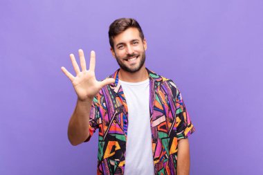 Genç adam gülümsüyor ve arkadaş canlısı görünüyor, 5 ya da 5 numarayı gösteriyor, eli önde, geriye doğru sayıyor.