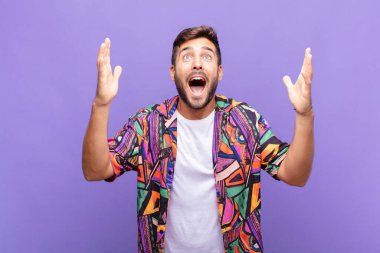 Genç adam mutlu, şaşkın, şanslı ve şaşırmış hissediyor, zaferi kutluyor, iki eli havada.