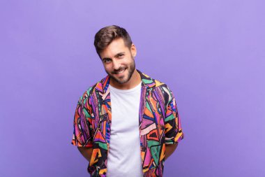 Genç adam gururlu, kendinden emin, havalı, küstah ve küstah görünüyor, gülümsüyor, başarılı hissediyor.