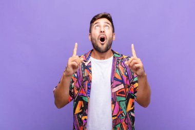 Genç adam şaşırmış, şaşırmış ve ağzı açık bir şekilde iki eliyle uzayı göstererek uzayı kopyalıyor.