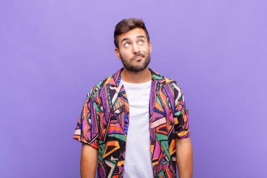 Genç adam şaşkın ve şaşkın görünüyor, merak ediyor veya bir sorunu çözmeye çalışıyor ya da düşünüyor.