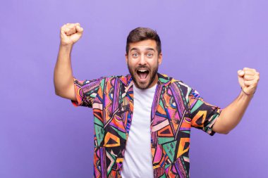 Genç adam muzaffer bir şekilde bağırıyor, heyecanlı, mutlu ve şaşırmış görünüyor.