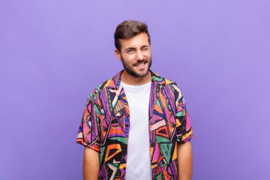 Genç adam mutlu ve arkadaş canlısı görünüyor, gülümsüyor ve sana olumlu bir tavırla göz kırpıyor.